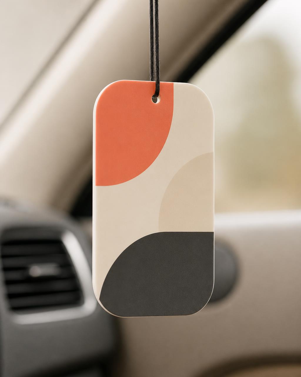 Close detail of an unbranded hanging air freshener with simple abstract artwork in a neutral vehicle interior.