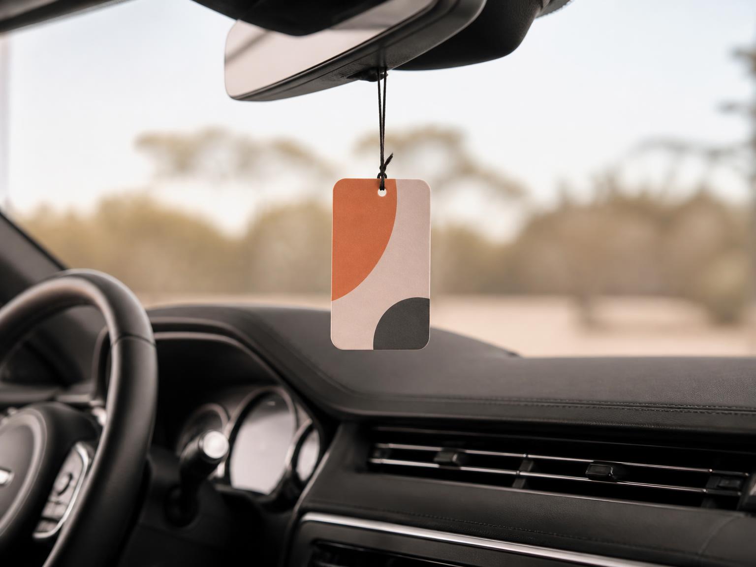 Unbranded custom hanging air freshener with abstract artwork in a softly lit vehicle interior.