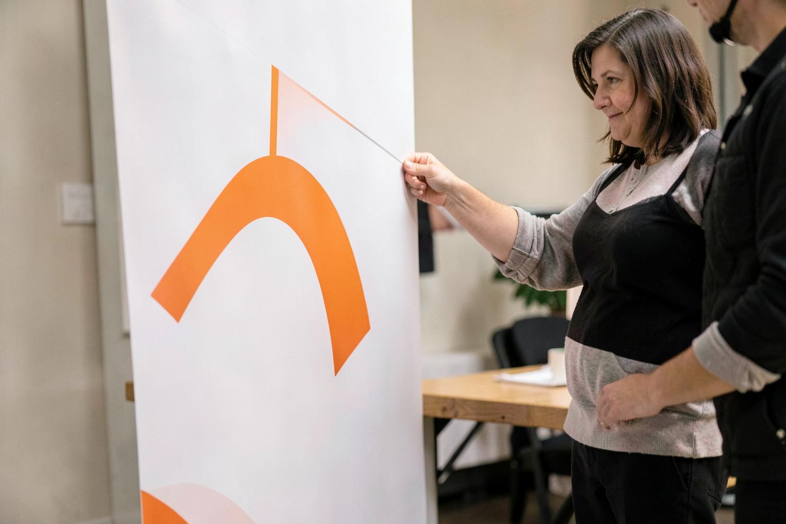 Adult raising a retractable banner with an abstract orange arc design.